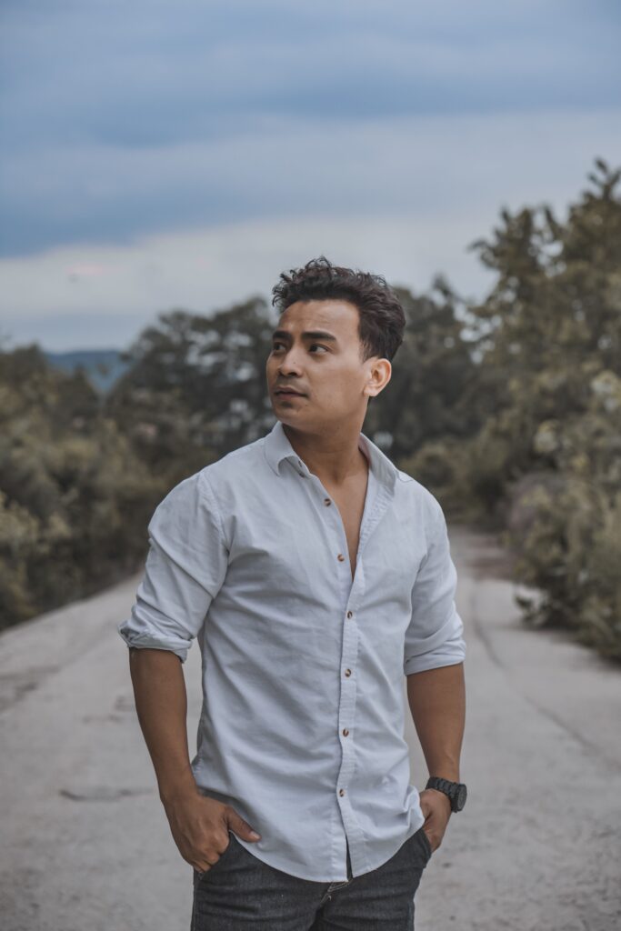 avatar_on_about A man in casual white shirt and jeans posing confidently on a rural road with trees around.